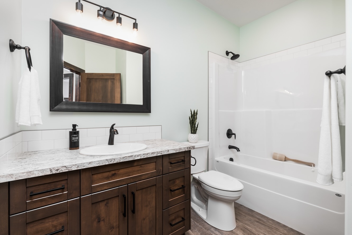 Stylish bathroom featuring a wooden vanity with a marble countertop, a large mirror, and modern fixtures. A white bathtub with towels and a small plant add elegance.