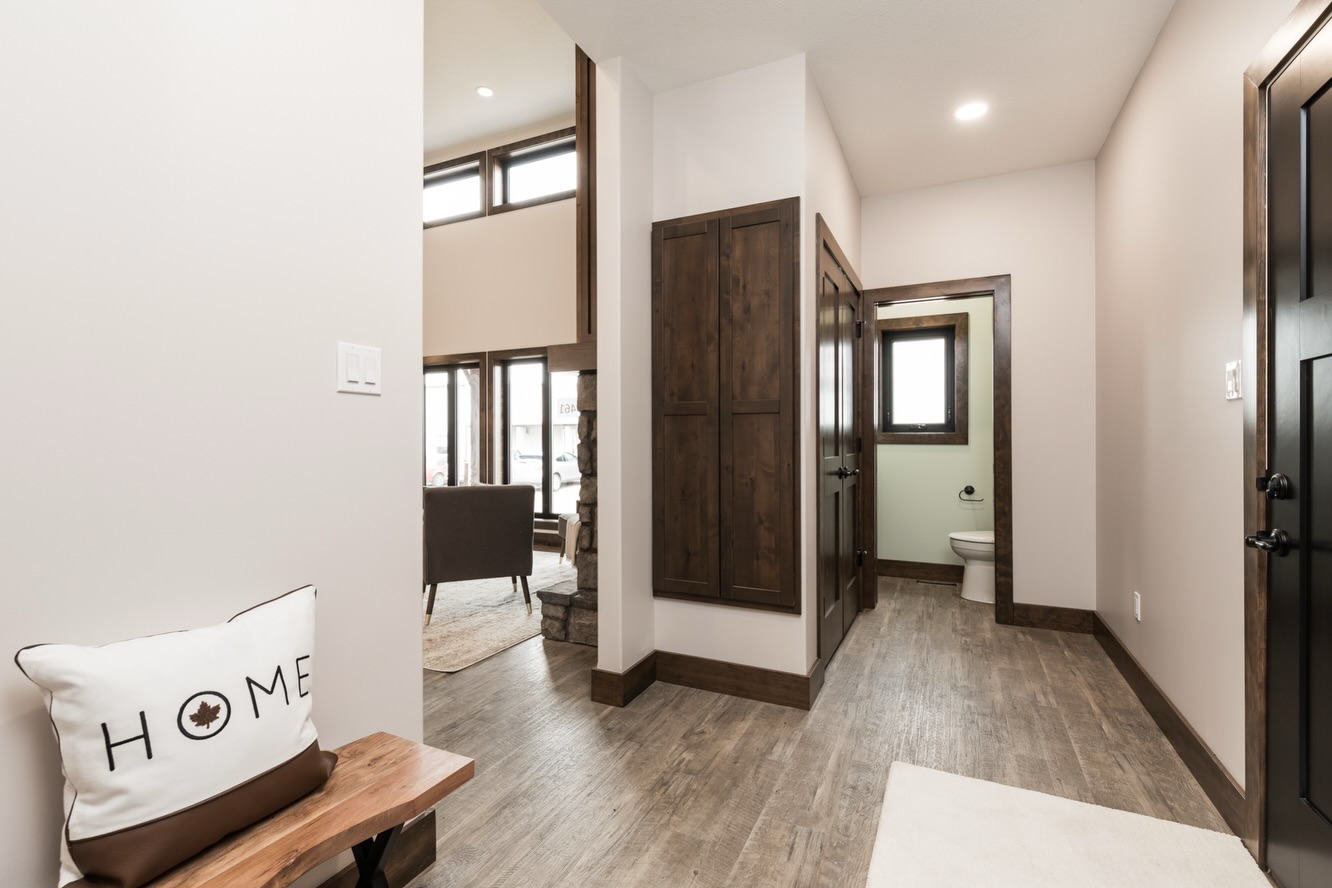 Modern interior hallway with wooden floors and white walls. A bench with a "Home" pillow is on the left. A bathroom is visible ahead.