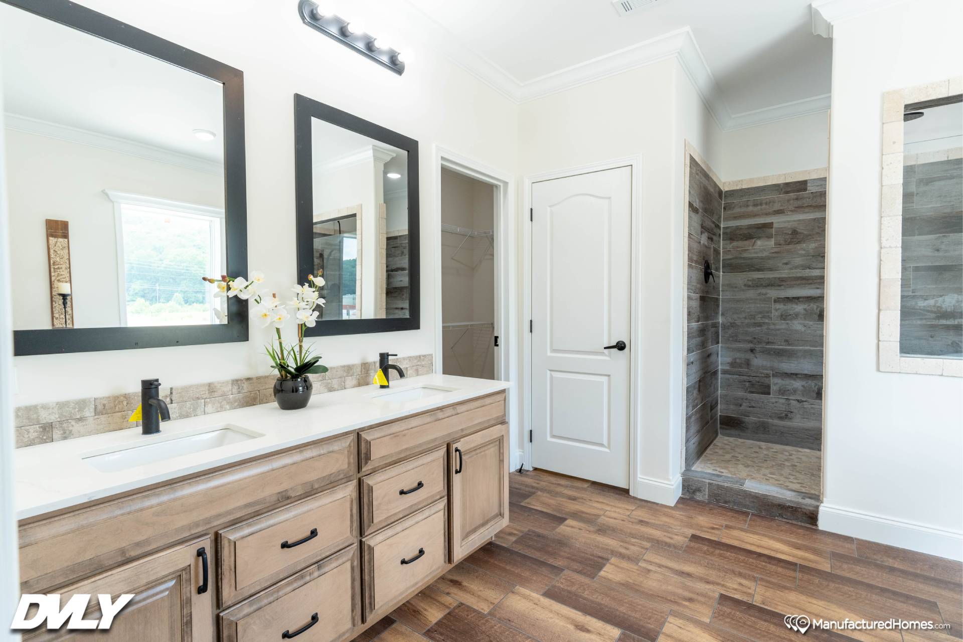 Modern bathroom with a double vanity featuring wood cabinets and two large mirrors. There is a potted plant on the counter and a walk-in tiled shower.