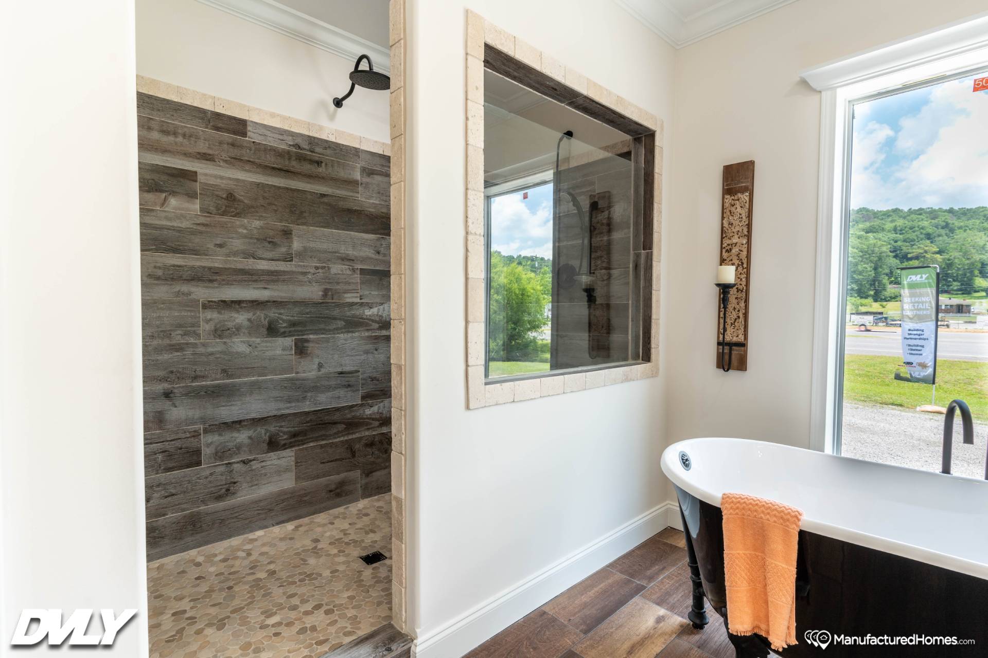Modern bathroom featuring a rustic wood-paneled shower, freestanding tub with an orange towel, large window with green landscape view, and serene ambiance.
