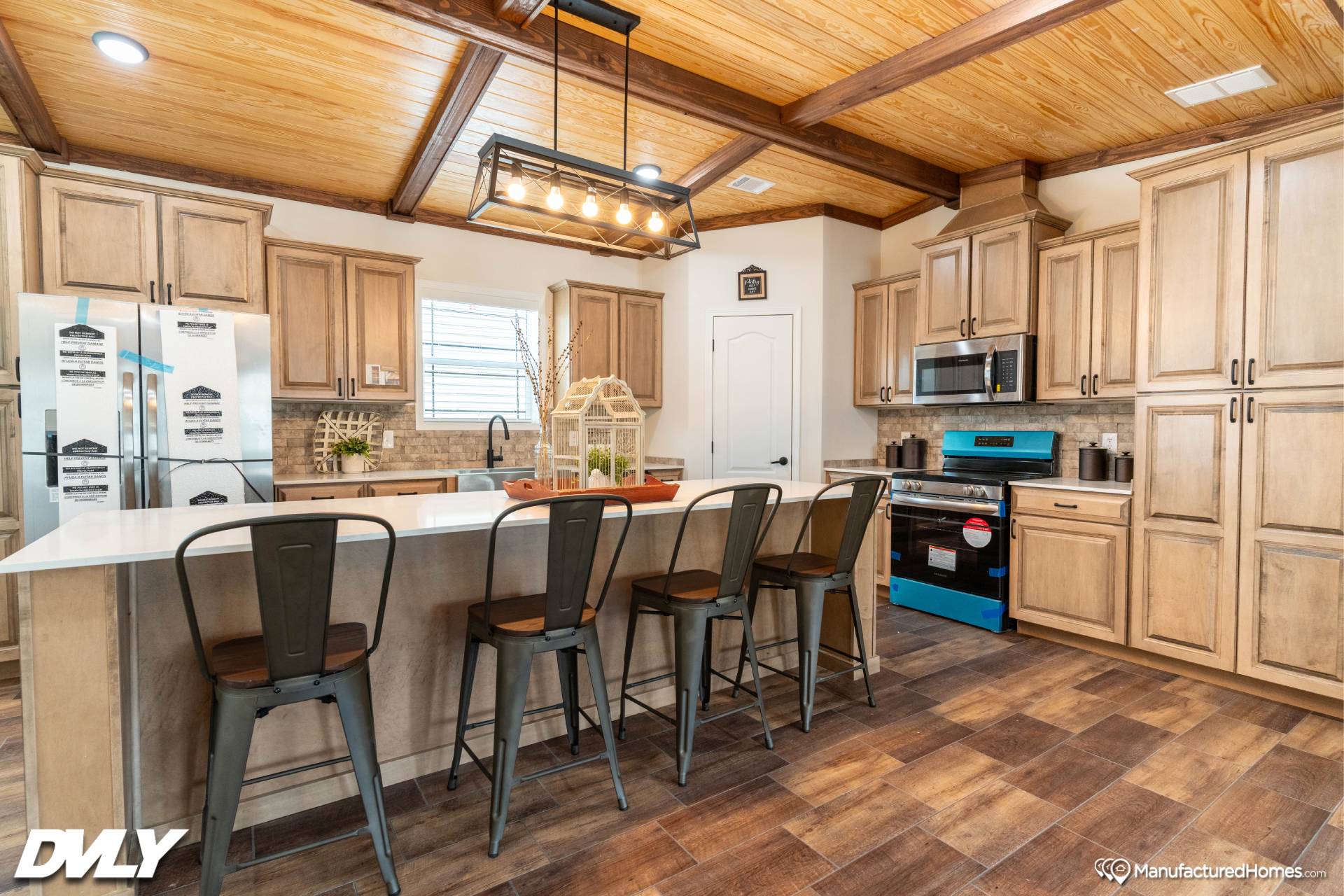 Warm, rustic kitchen with wooden cabinets, large island, and metal-stool seating. Features exposed beams, hanging lights, and modern appliances. Cozy ambiance.