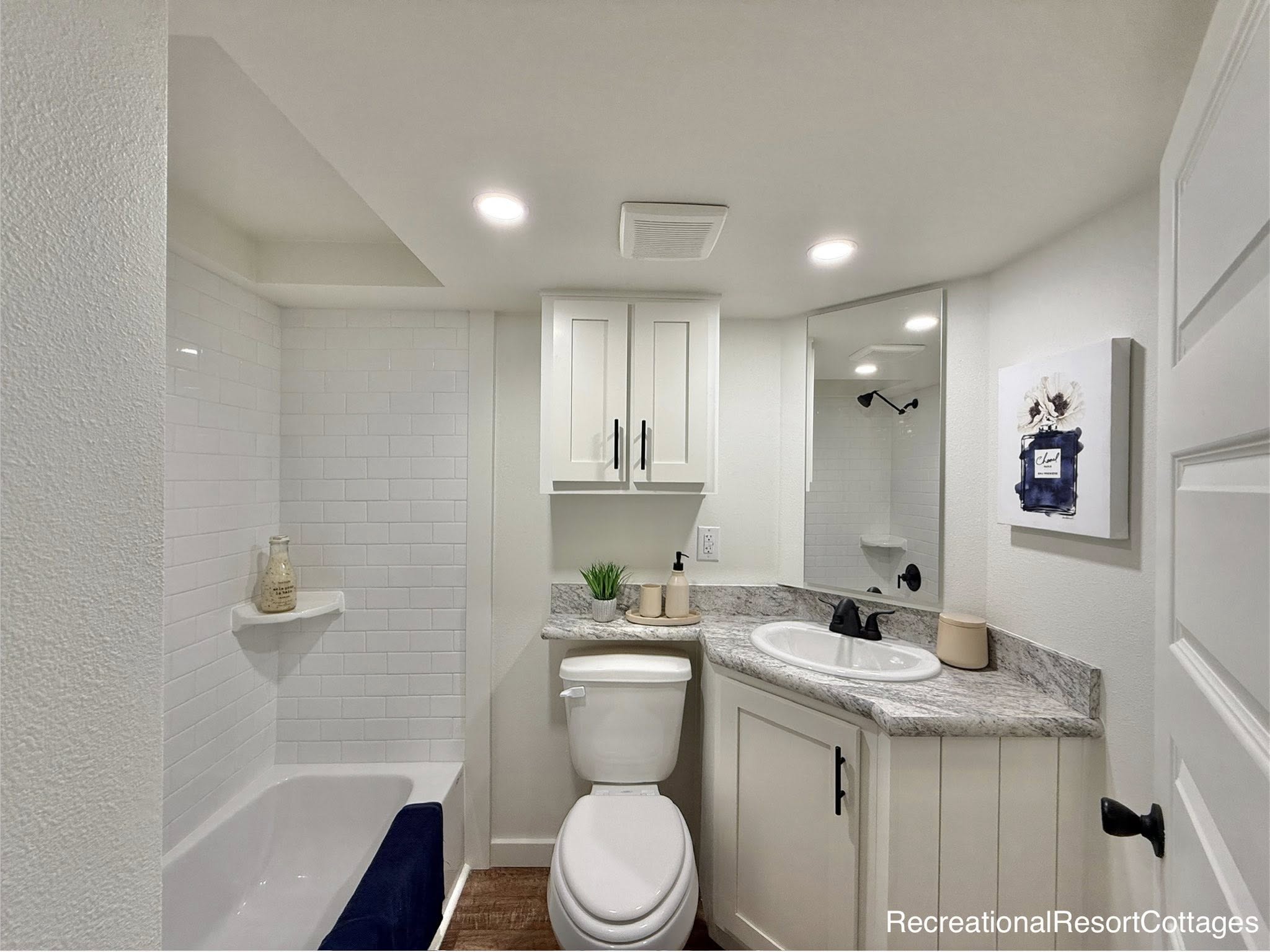 Modern bathroom with a corner granite countertop, white sink, and cabinet. White tiled shower, potted plant, and decor create a clean, cozy feel.