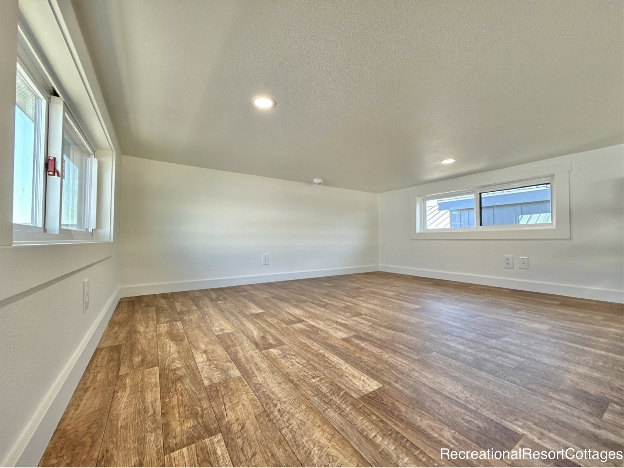 Bright, minimalist loft with light wood flooring, white walls, and two rectangular windows. The space feels cozy and inviting, enhanced by warm lighting.