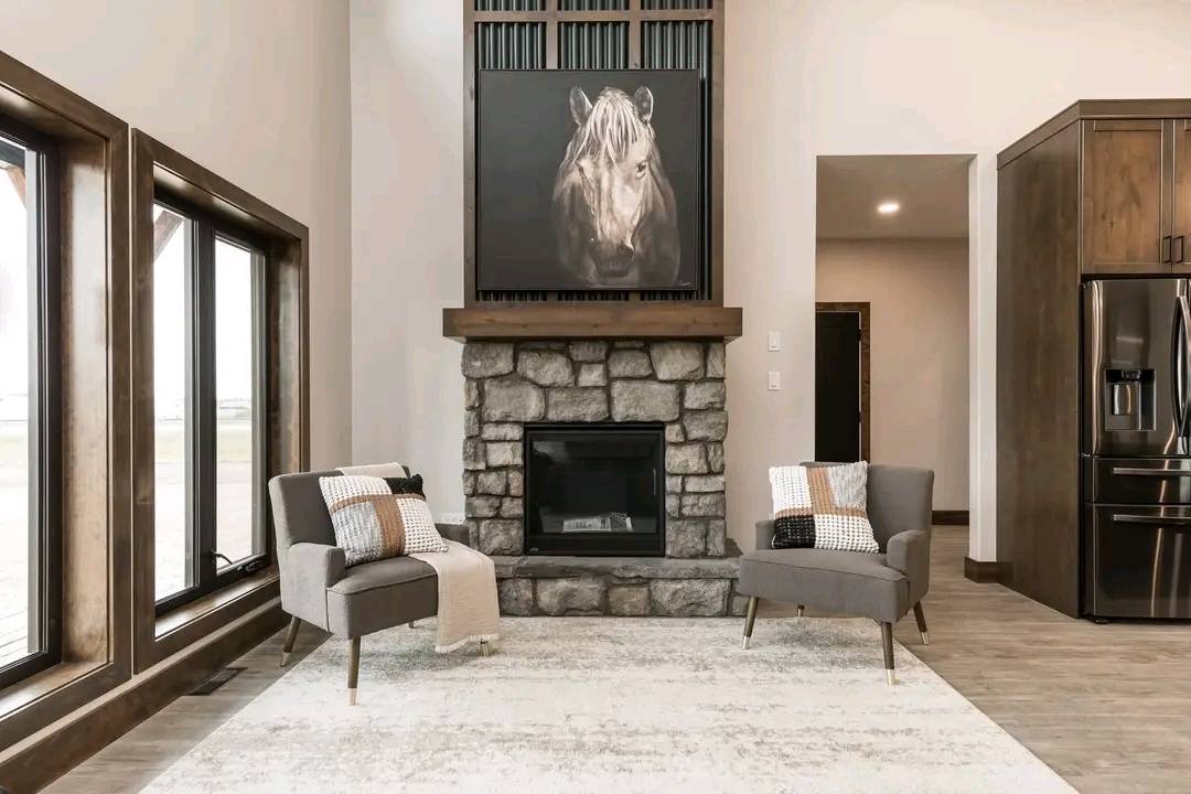 A cozy living room featuring a stone fireplace with a horse painting above it, flanked by two gray armchairs with cushions and blankets, creating a serene ambiance.