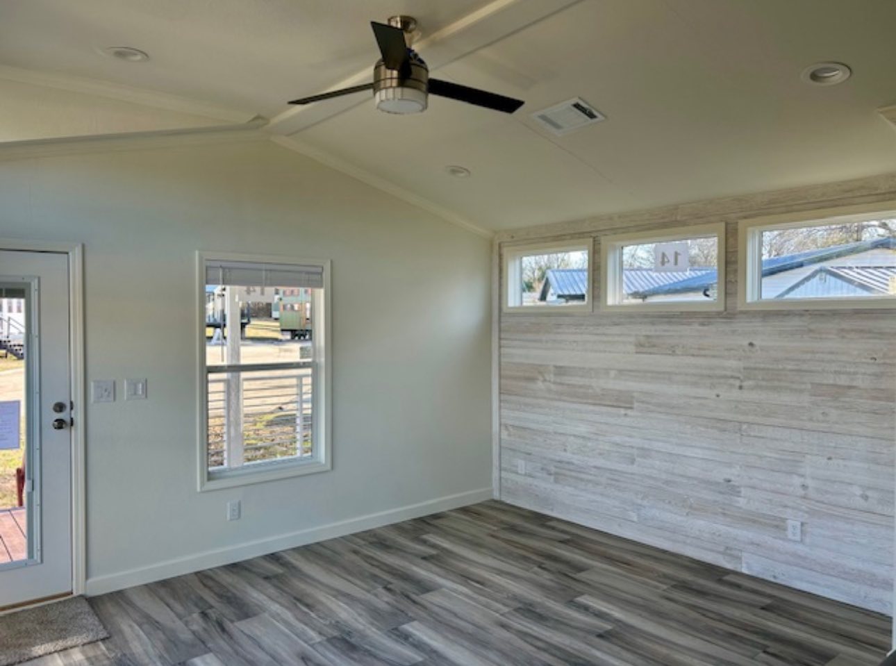Small room interior with light wood flooring, white walls, and a wood accent wall. There are three narrow windows and a ceiling fan, creating a bright, airy vibe.