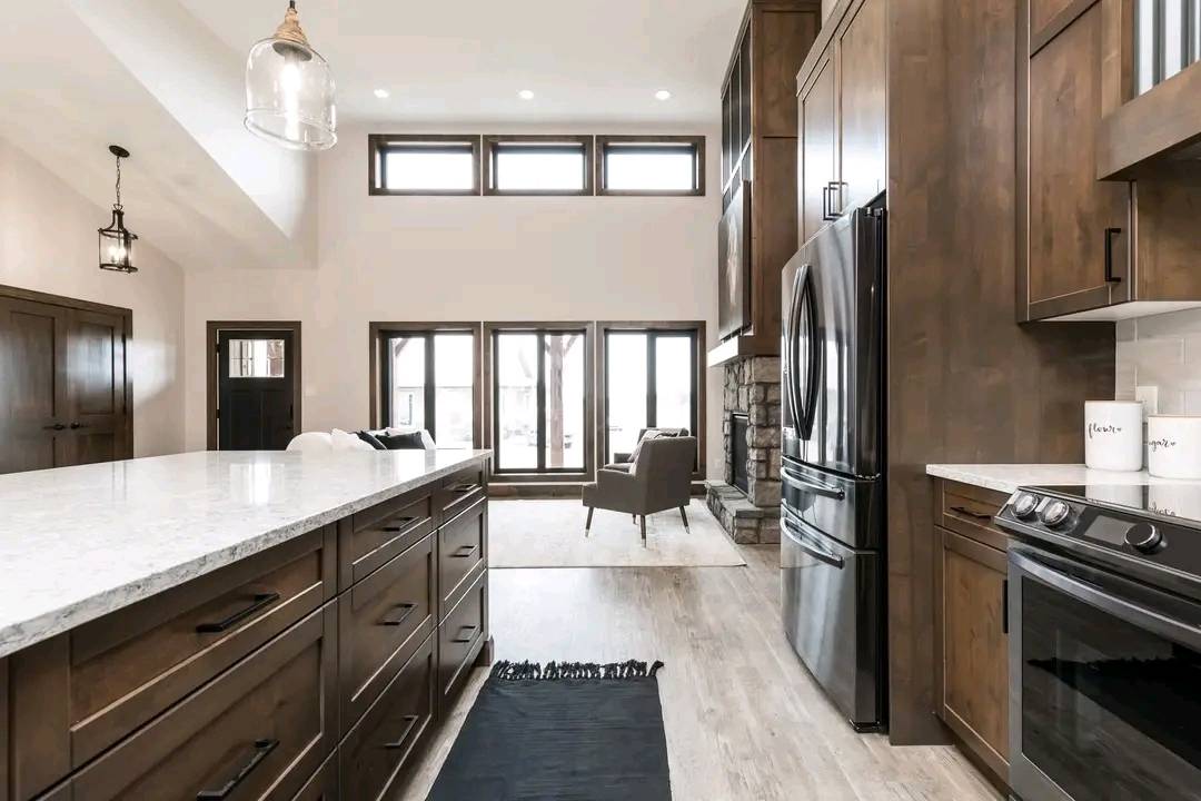 Modern kitchen with wood cabinetry, marble countertops, and stainless steel appliances. Large windows provide natural light. The space is bright and welcoming.