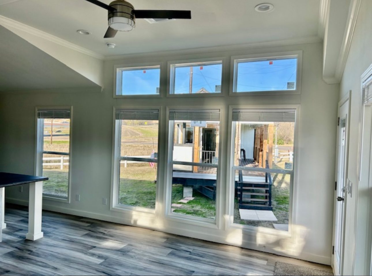Spacious room with large windows and a ceiling fan, offering a bright view of a patio and grassy lawn. Light wood flooring adds warmth.