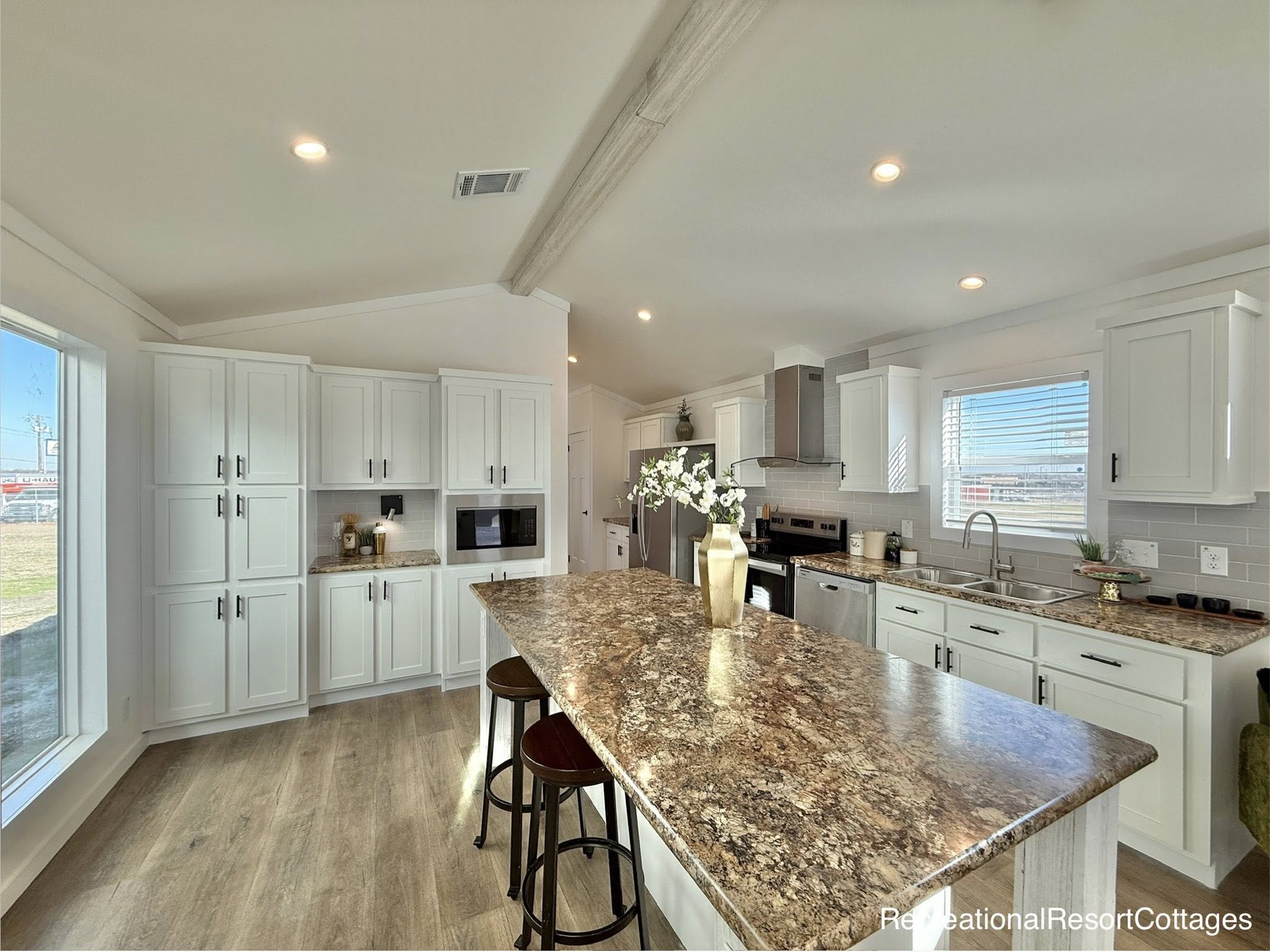 Bright, modern kitchen with white cabinets, marbled island, and stainless steel appliances. Sunlight streams through a large window, creating a welcoming ambiance.
