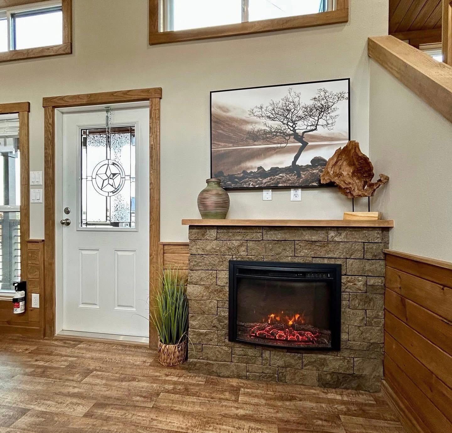 Cozy interior with a white door featuring stained glass, a stone fireplace with a glowing electric fire, and decorative items, creating a warm ambiance.