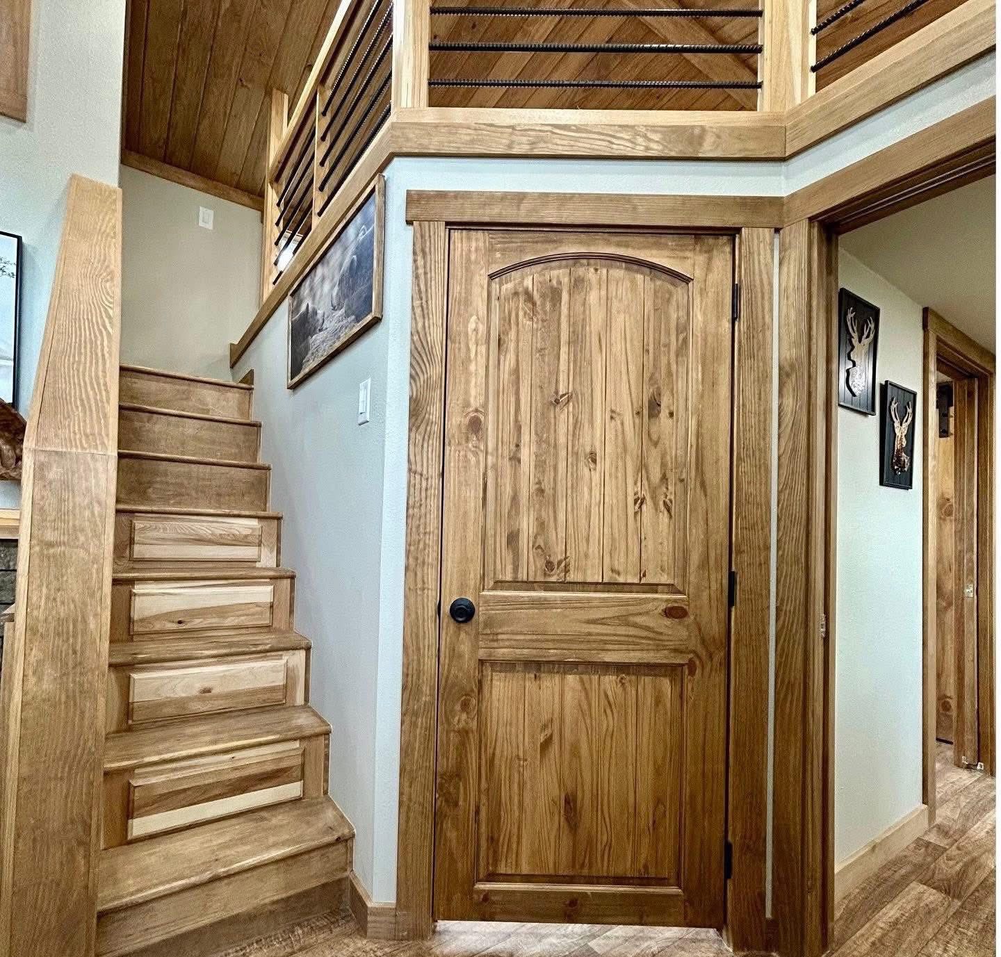 Wooden staircase and door with rustic charm, warm tones. Wall art of deer heads adds a cozy, cabin-like atmosphere. Wooden railing enhances the aesthetic.