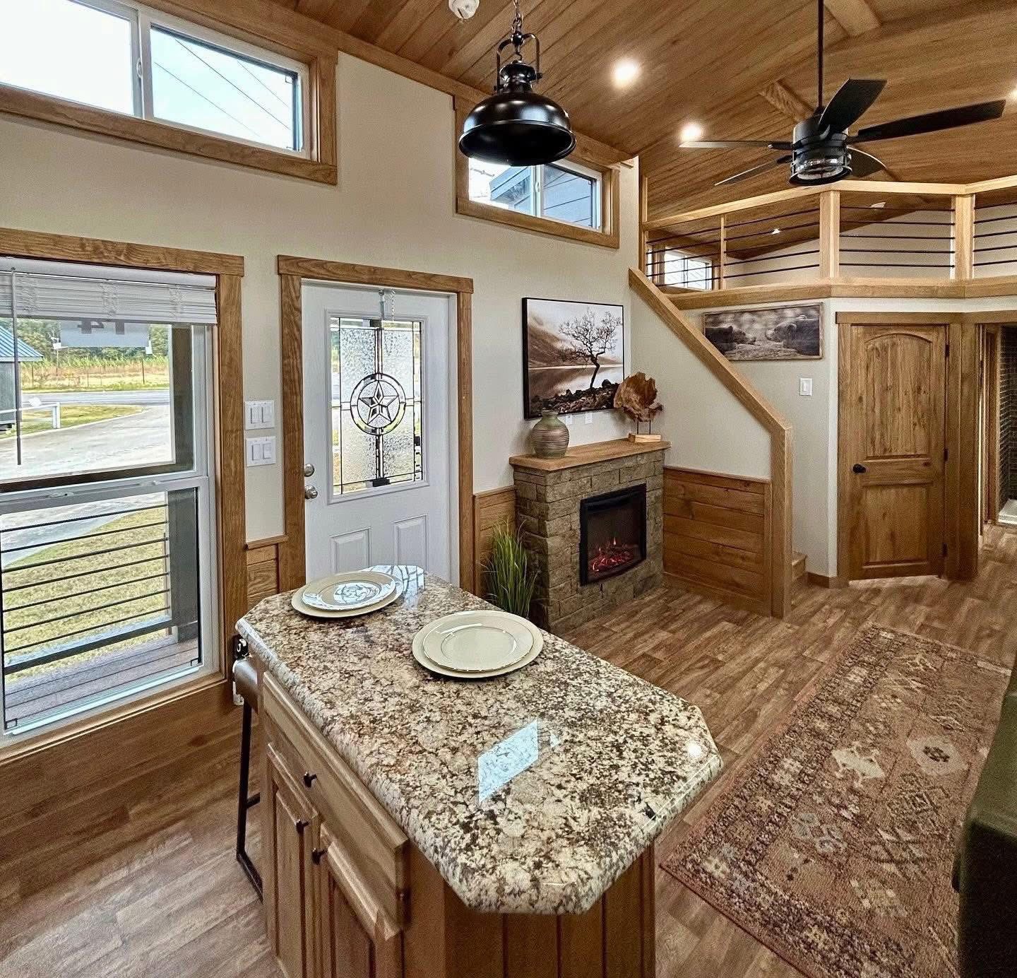 Compact living room with wooden accents, a granite kitchen island, and a warm fireplace. Natural light streams through the door and windows, creating a cozy, inviting atmosphere.