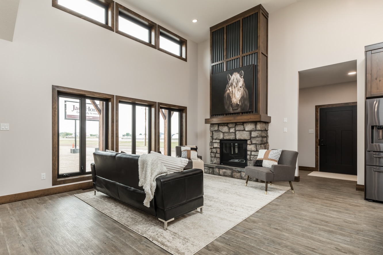 Spacious living room with high ceilings and wood flooring. Features a stone fireplace, large windows, leather couch, and horse artwork, conveying elegance.
