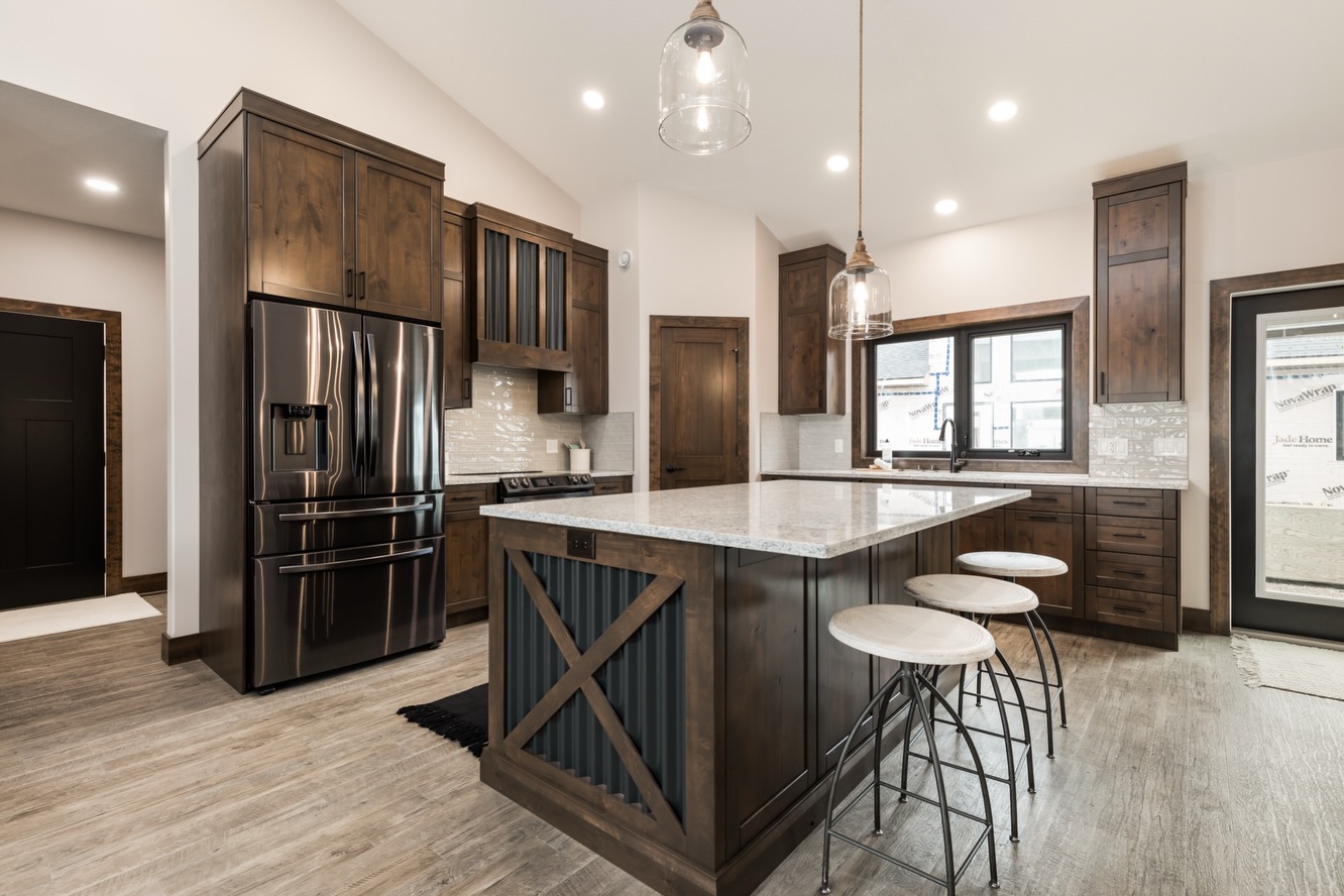 Spacious kitchen with dark wood cabinets, stainless steel fridge, and a large island with bar stools. Pendant lights and a bright window create a warm, modern feel.