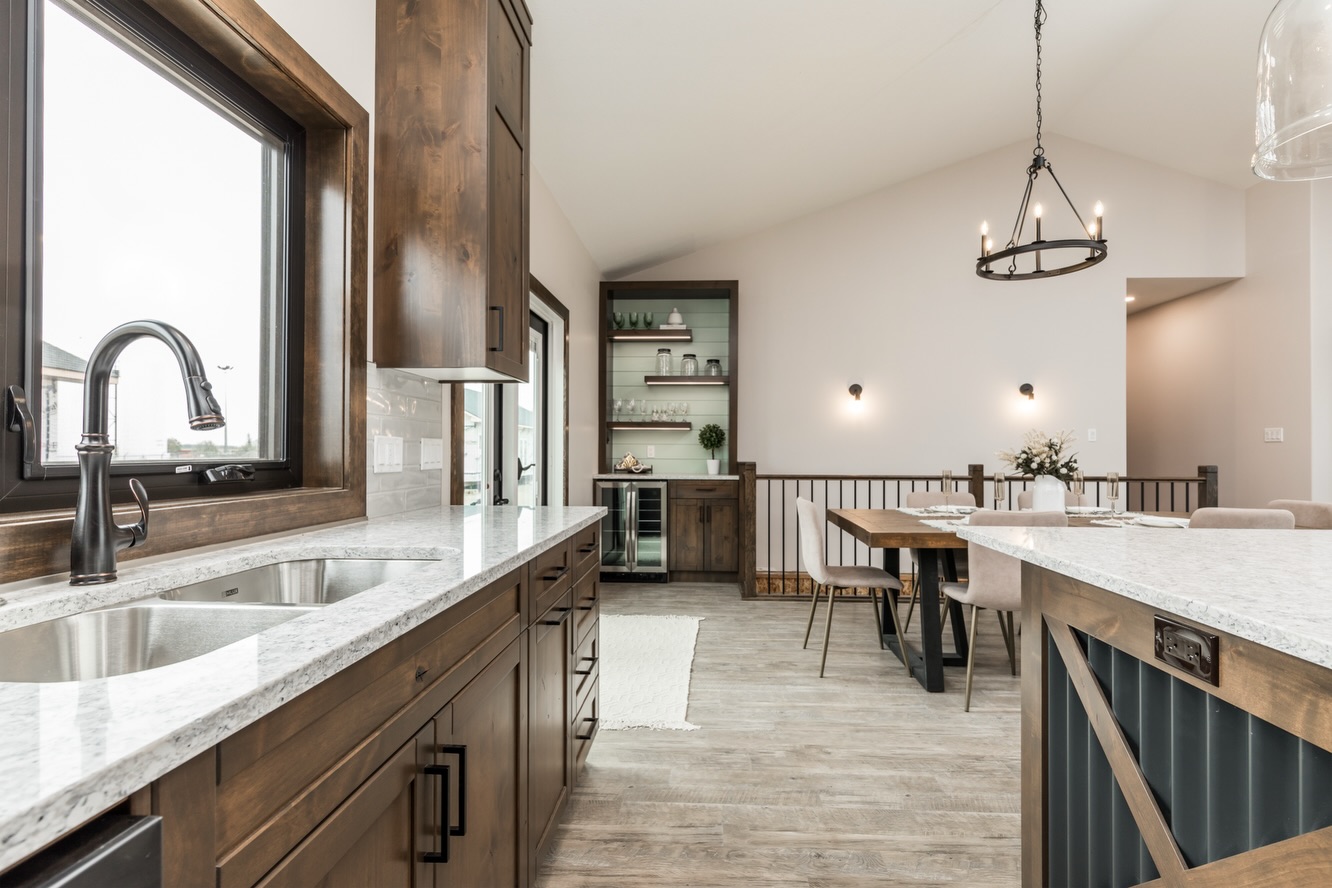 Modern kitchen with a rustic touch featuring wooden cabinets and granite countertops. An open dining area with a wooden table and chandelier adds elegance.