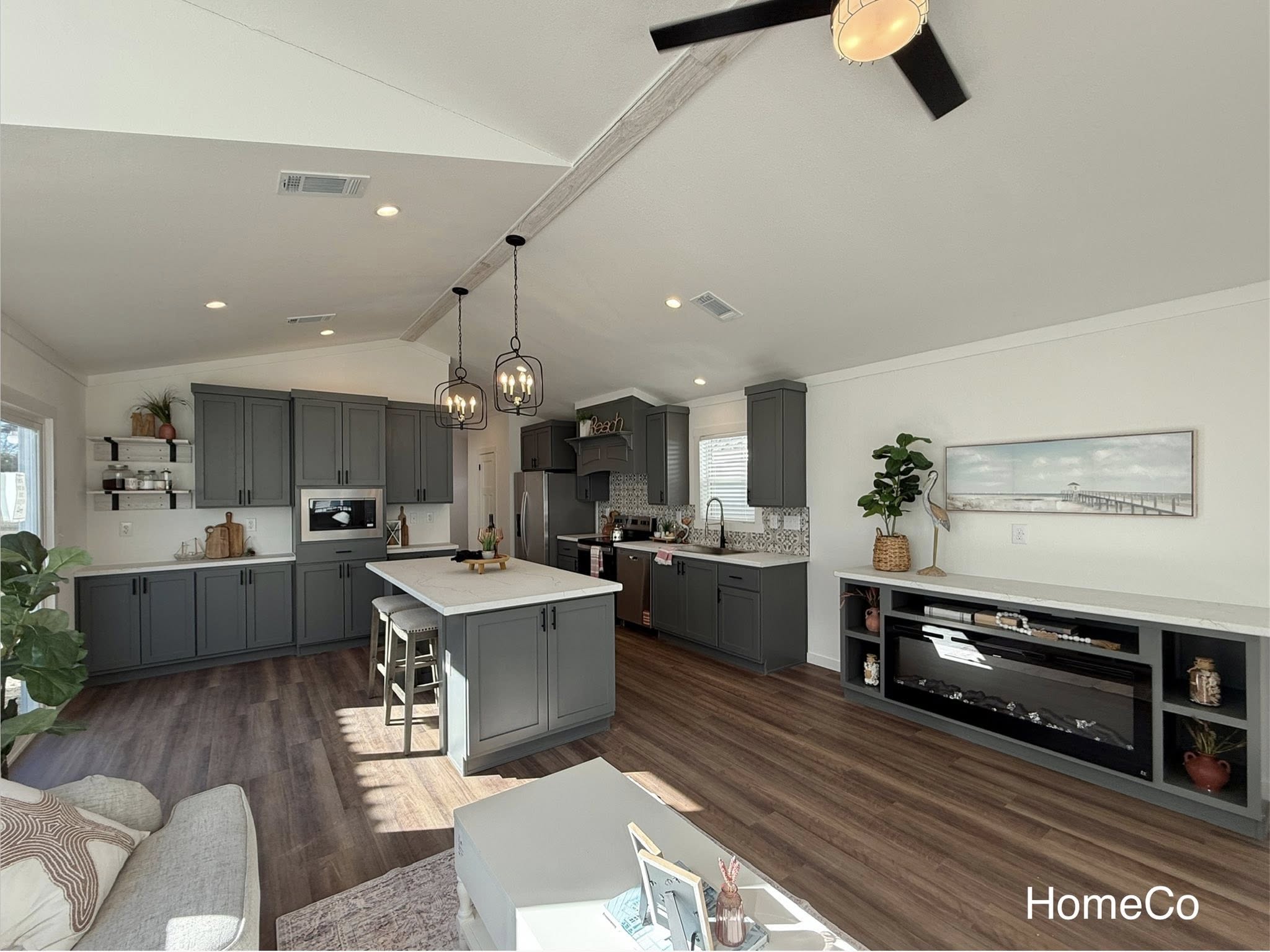 Modern kitchen in neutral tones features gray cabinets, a central island with pendant lights, wood flooring, and decor accents, creating a cozy ambiance.