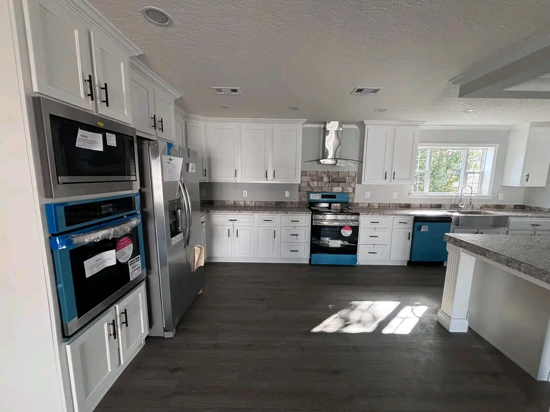 Modern kitchen with white cabinets, stainless steel appliances, and dark wood flooring. Sunlight streams through a window, creating a cozy ambiance.