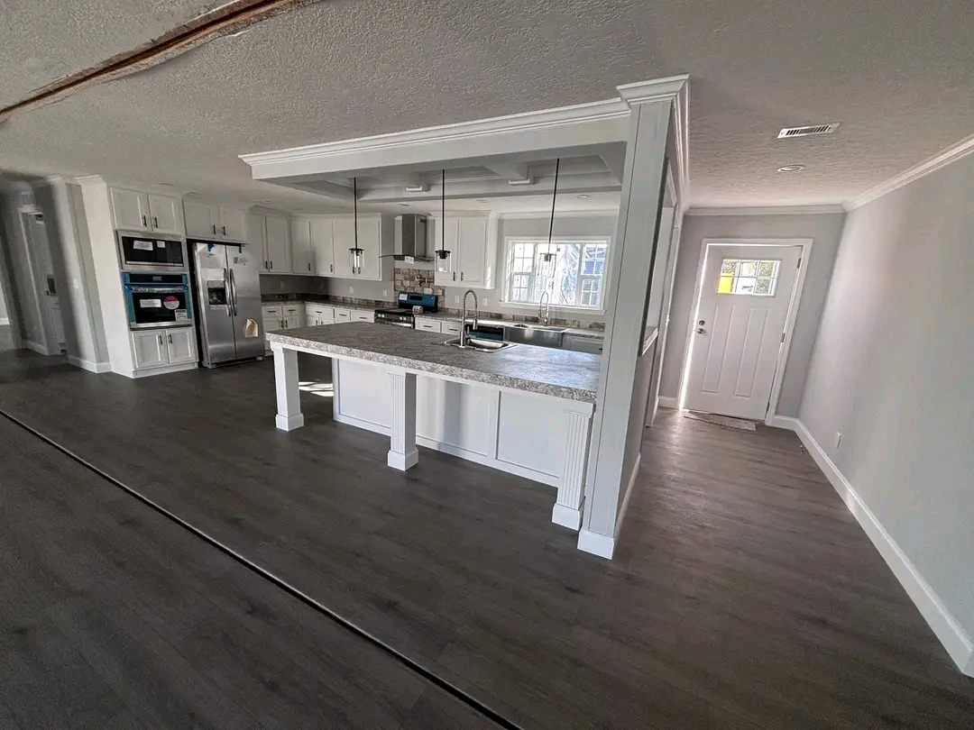 Modern kitchen and hallway with dark wood floors, white cabinets, and stainless steel appliances. Natural light from a window creates an inviting atmosphere.