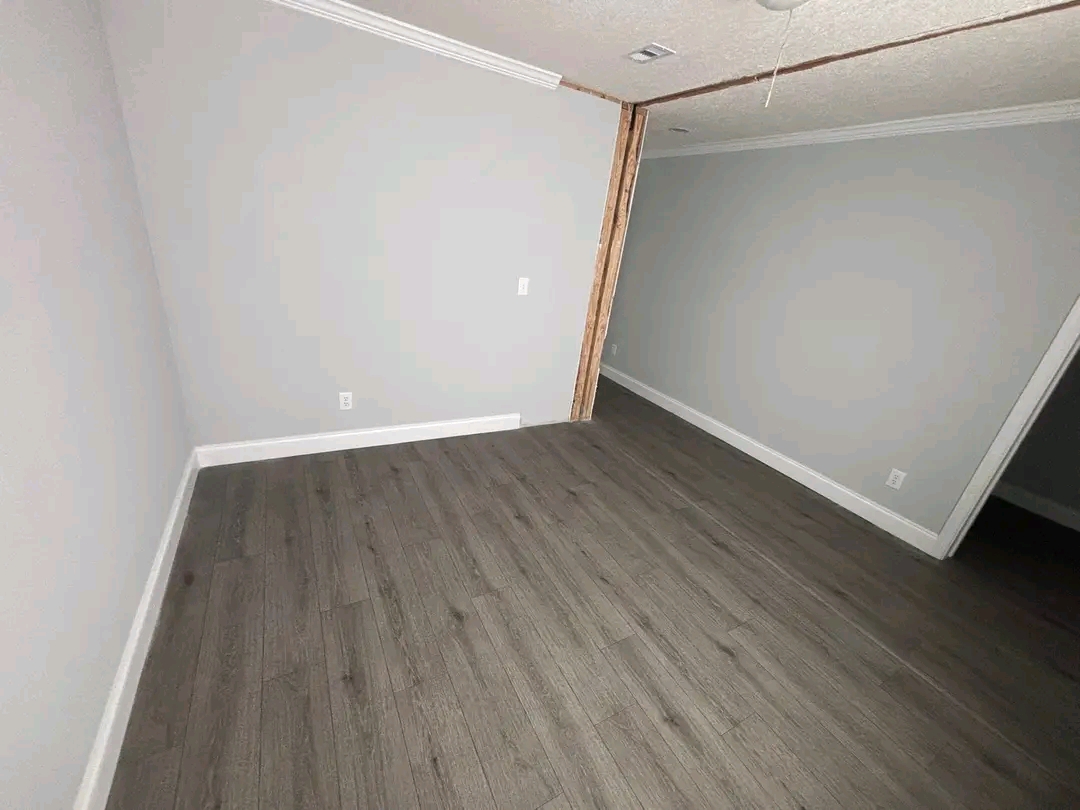 A small, unfurnished room with light gray walls and dark wood flooring. The space has a simple, clean look, evoking a sense of modern minimalism.