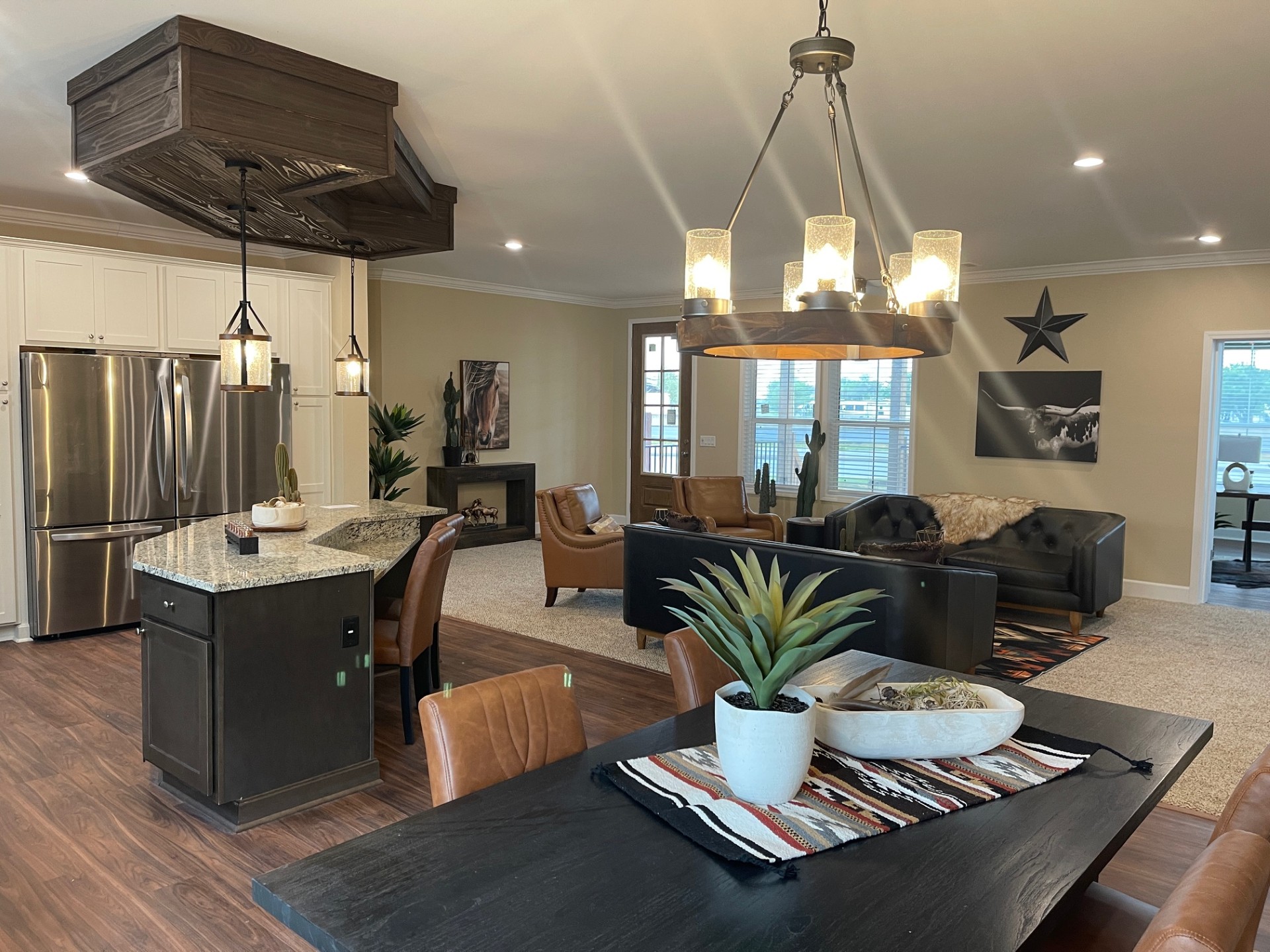 Open-concept living room and kitchen with rustic-modern decor. Features a black dining table with plants, pendant lights, leather seating, and wood accents. Cozy and inviting atmosphere.
