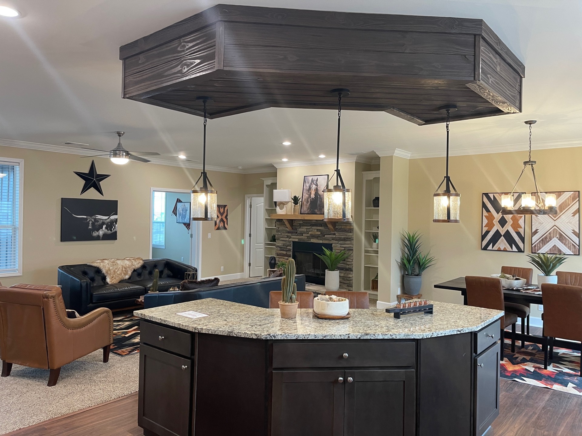 Spacious open-plan living area with modern farmhouse decor. Features a kitchen island, pendant lights, leather chairs, dark sofas, and geometric artwork.