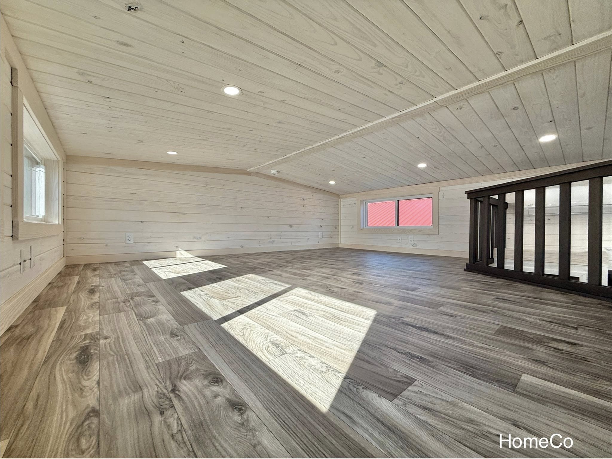 Spacious loft with light wood paneling, recessed lighting, large windows, and laminate flooring. Bright and airy, conveying a cozy feel.
