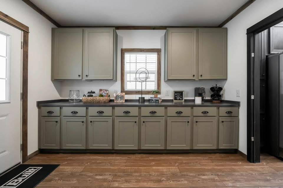 Cozy kitchen with gray cabinets, black countertop, and wooden floor. A window with blinds centers the wall, adding natural light and warmth.
