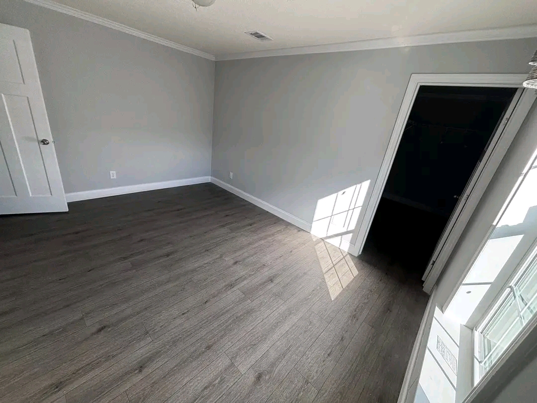 Empty room with light gray walls and wood laminate flooring. Sunlight streams through a window, casting a geometric shadow on the floor. Calm and minimalist.
