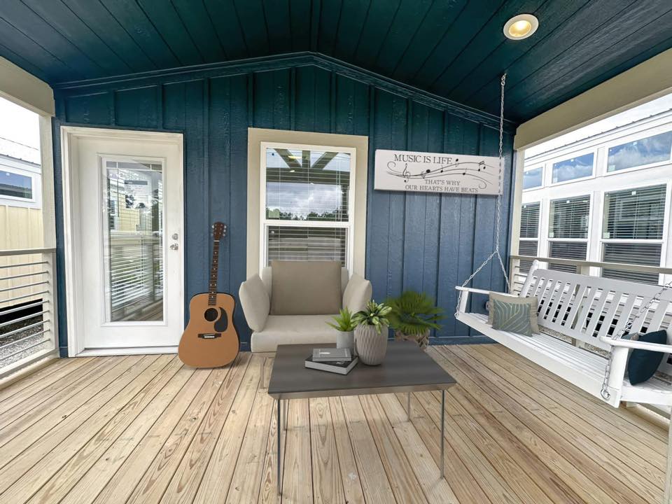 Cozy porch with a wooden floor, blue walls, and ceiling. Features a white swing, guitar, potted plant on a table, and a sign: "Music is Life."