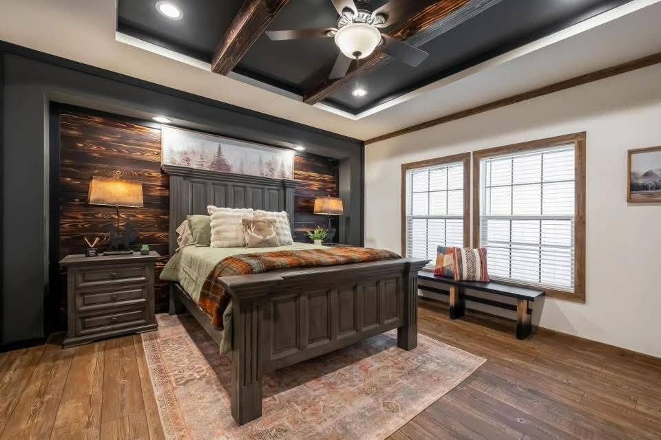 Rustic bedroom with a large wooden bed, flanked by lamps on nightstands. A cozy bench and windows enhance the warm, inviting atmosphere.