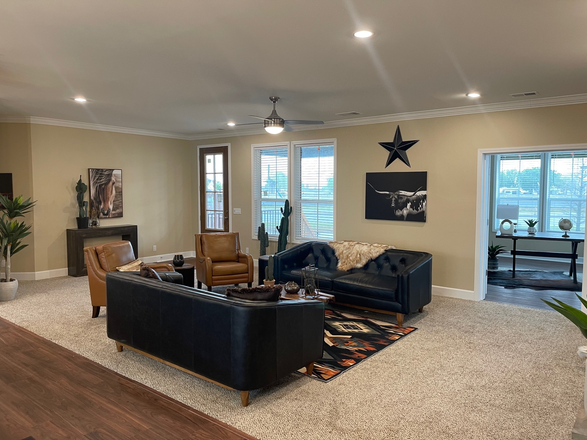 Stylish living room with a beige carpet, navy blue sofa, brown leather chairs, a cowhide rug, and Western decor. Bright windows and neutral tones.