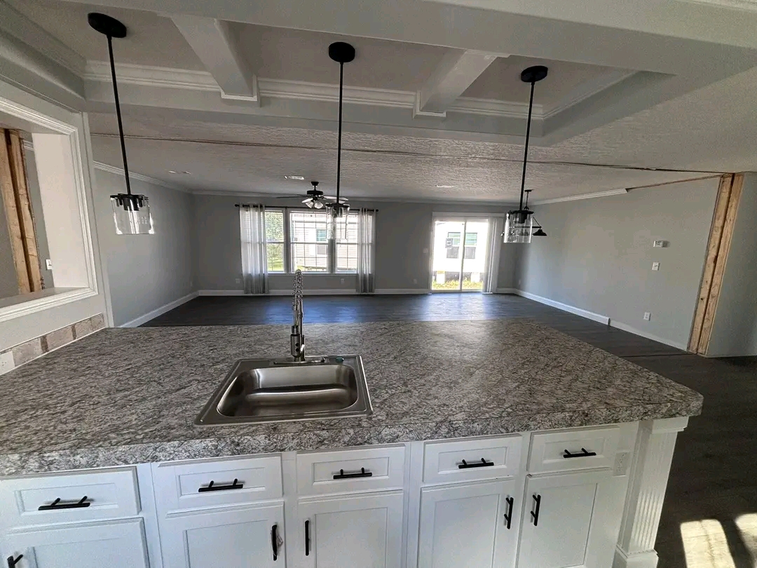 Spacious, modern open-plan kitchen and living area featuring a granite countertop, stainless steel sink, pendant lights, and large windows for natural light.