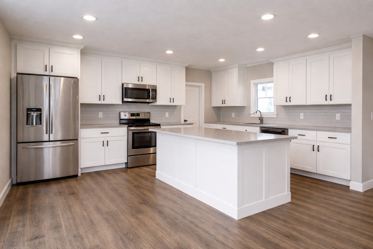 Modern kitchen with white cabinets, stainless steel appliances, and a central island on wood flooring. Bright lighting creates a clean, spacious feel.