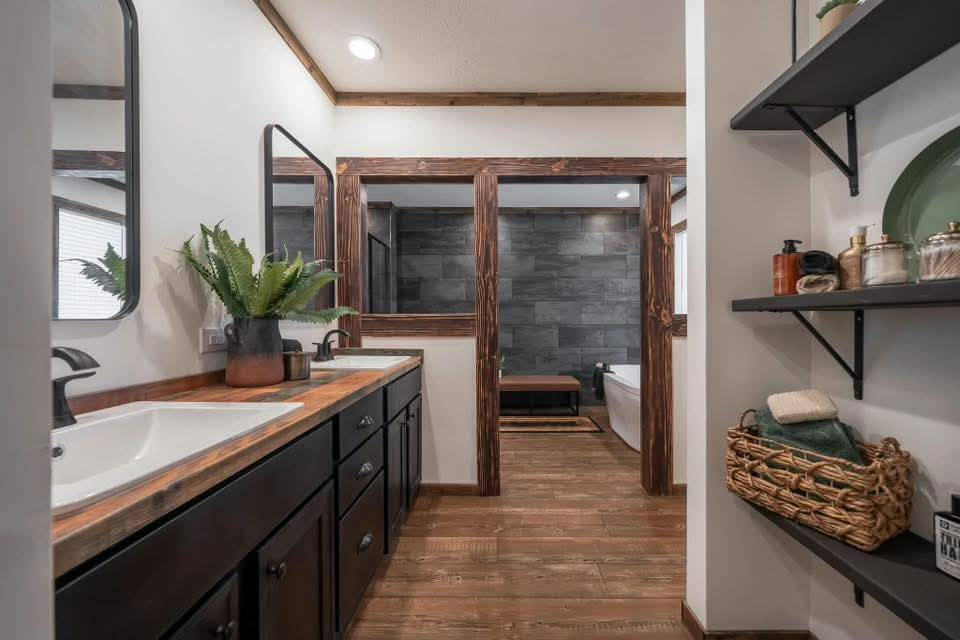 Modern rustic bathroom with dark wood cabinets and shelves, a double sink vanity, potted plant, and a freestanding tub against slate tiles. Cozy and elegant.