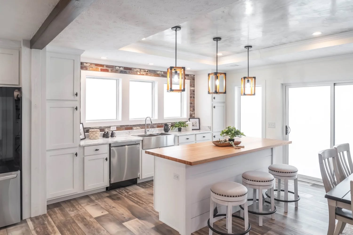 A modern kitchen featuring white cabinets, stainless steel appliances, and a wooden island with three stools. Pendant lights add warmth and style.