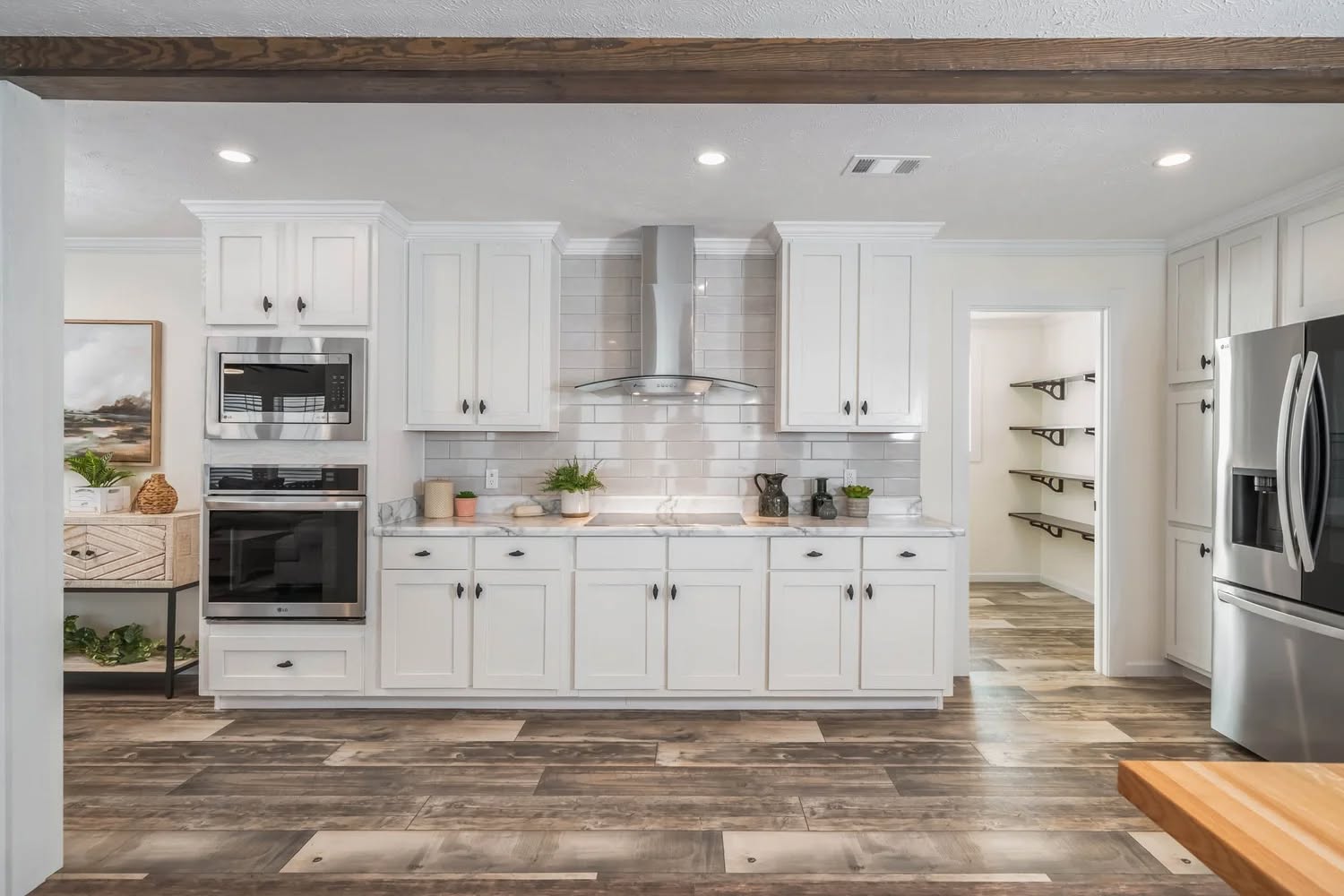 Modern kitchen with white cabinets, stainless steel appliances, and a wood-accented floor. The room is bright and organized, exuding a welcoming feel.