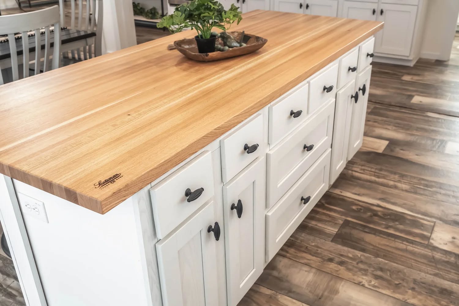 Kitchen island with a polished wooden countertop and white cabinets, featuring black handles. A wooden tray with a potted plant adds a natural touch.