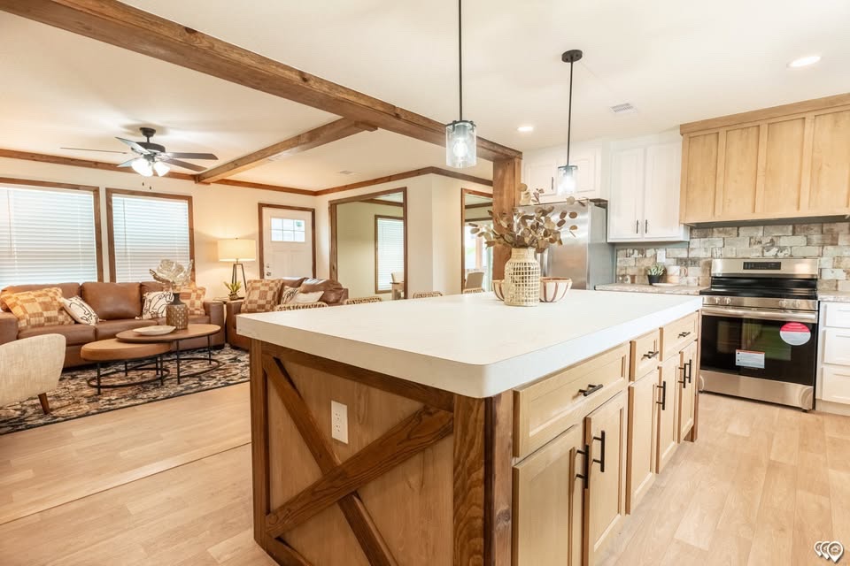 Spacious open-concept kitchen and living room with wooden beams. Features a large island, cozy brown leather sofas, and warm lighting, creating a welcoming atmosphere.