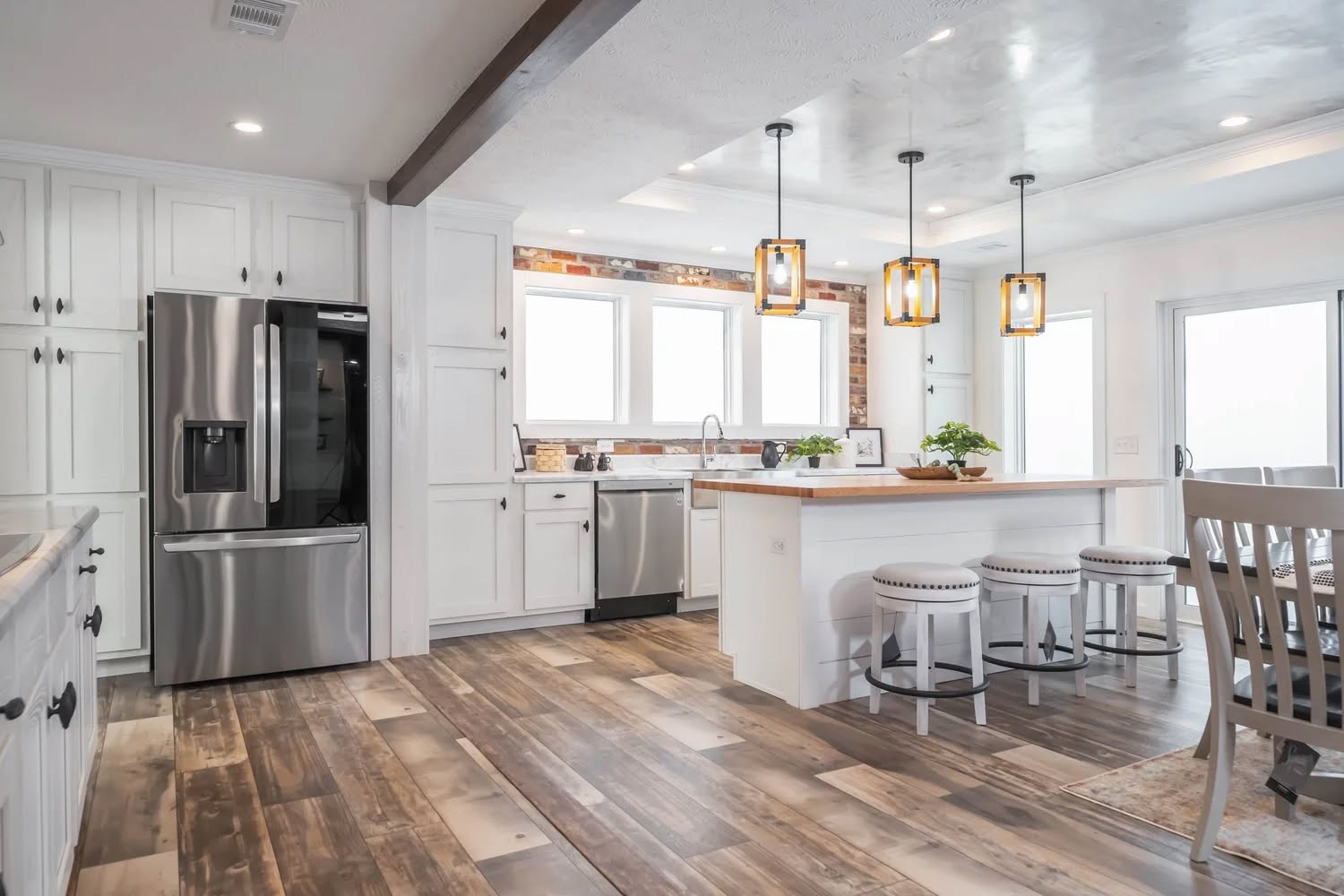 Modern kitchen featuring white cabinetry, stainless steel appliances, and wood flooring. A central island with bar stools and pendant lights adds warmth.