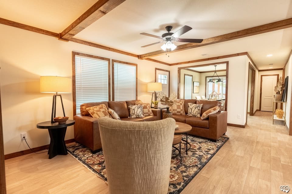 Warm, cozy living room featuring brown leather sofas, a beige armchair, wooden ceiling beams, soft lighting, and a patterned rug on hardwood floors.