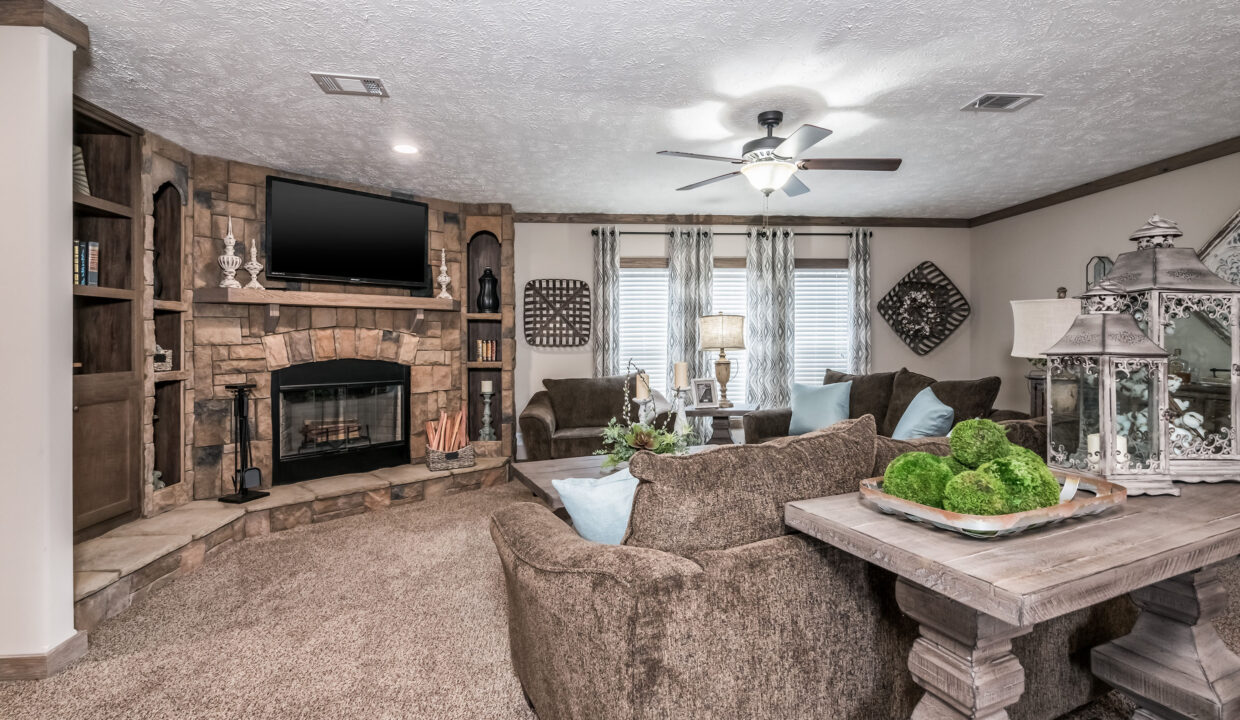 Cozy living room with brown sofas, stone fireplace with a TV, and soft lighting. Decor includes green plants, elegant lanterns, and patterned curtains.