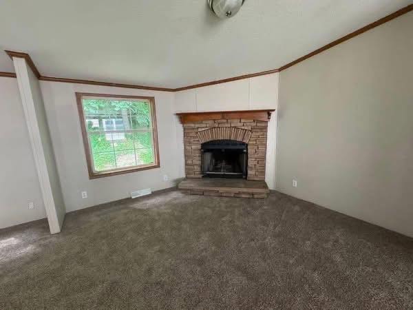 Spacious living room with neutral walls, carpeted floor, a brick fireplace, and a large window showcasing a green, leafy view, creating a cozy ambiance.