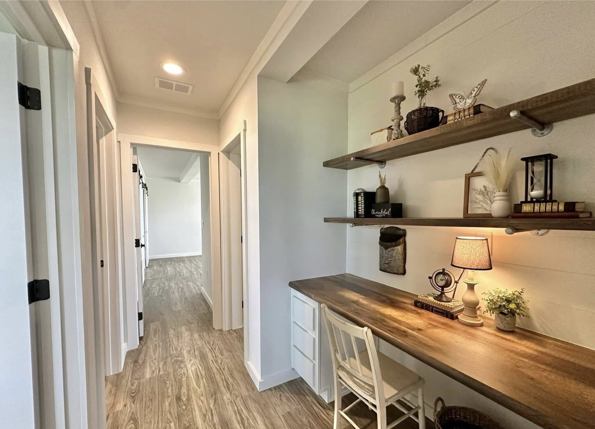 Cozy home office nook with wooden desk and chair, warmly lit by a lamp. Shelves above hold decorative items, creating a serene, productive space.