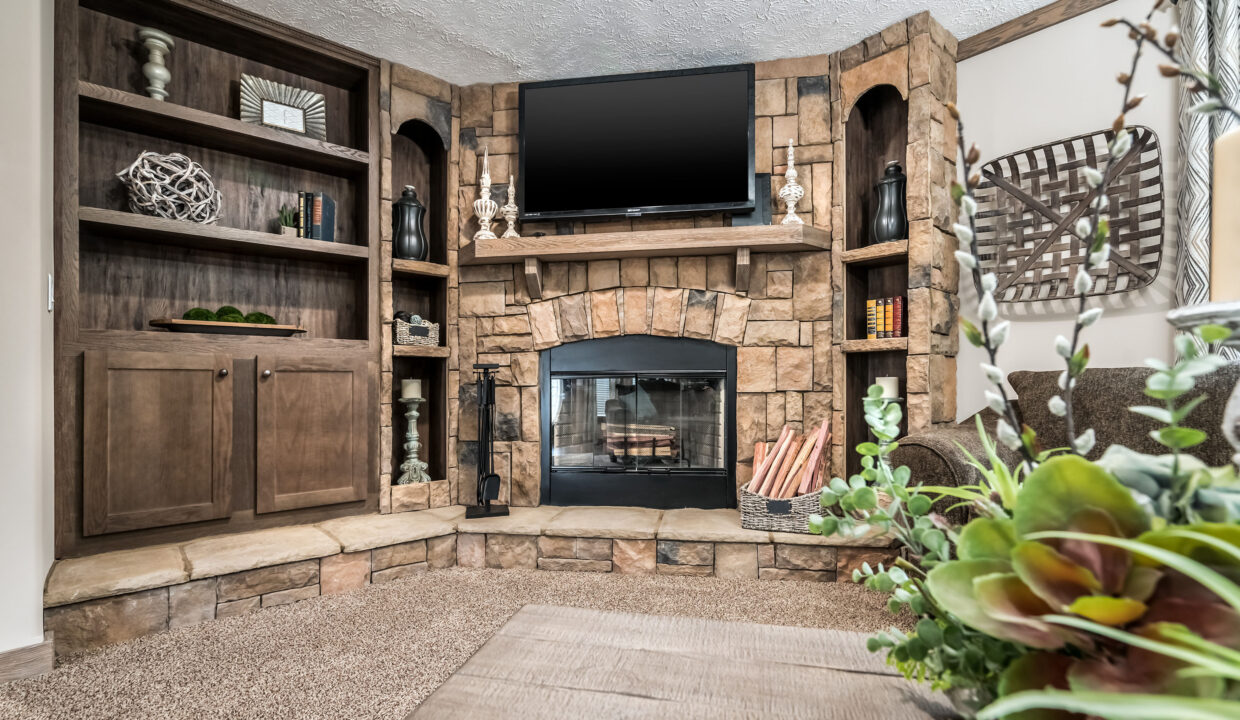 Cozy living room with a stone fireplace, wooden shelves, and a mounted TV. Decor includes plants and candles, creating a warm, inviting atmosphere.