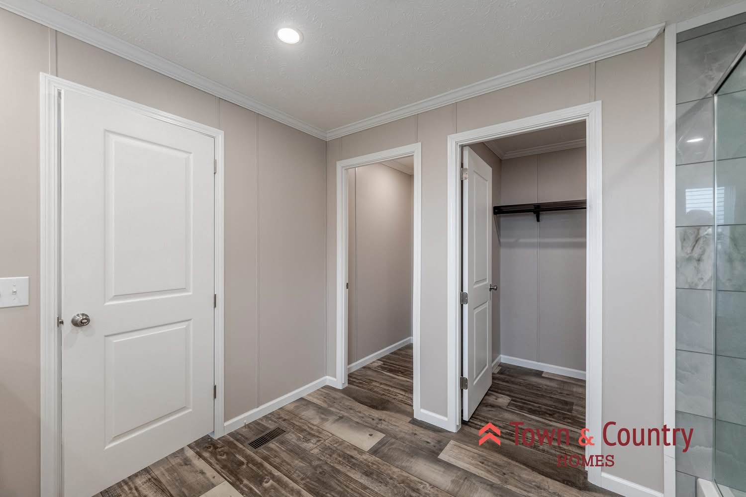 Bright hallway with wood-patterned flooring, beige walls, and white doors. One door opens to a walk-in closet. Modern and clean design.