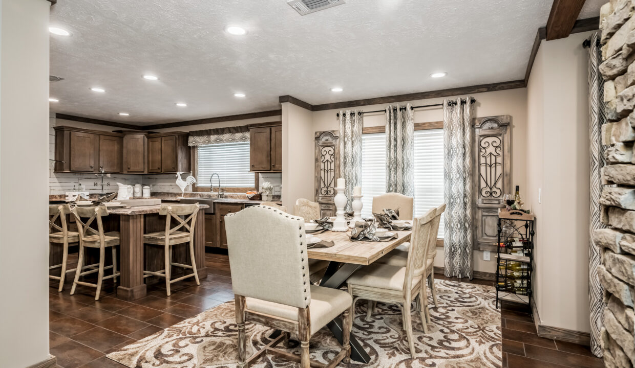 Warm-toned kitchen and dining area with wooden cabinets, patterned rug, elegant dining table, and plush chairs. Cozy, inviting ambiance.