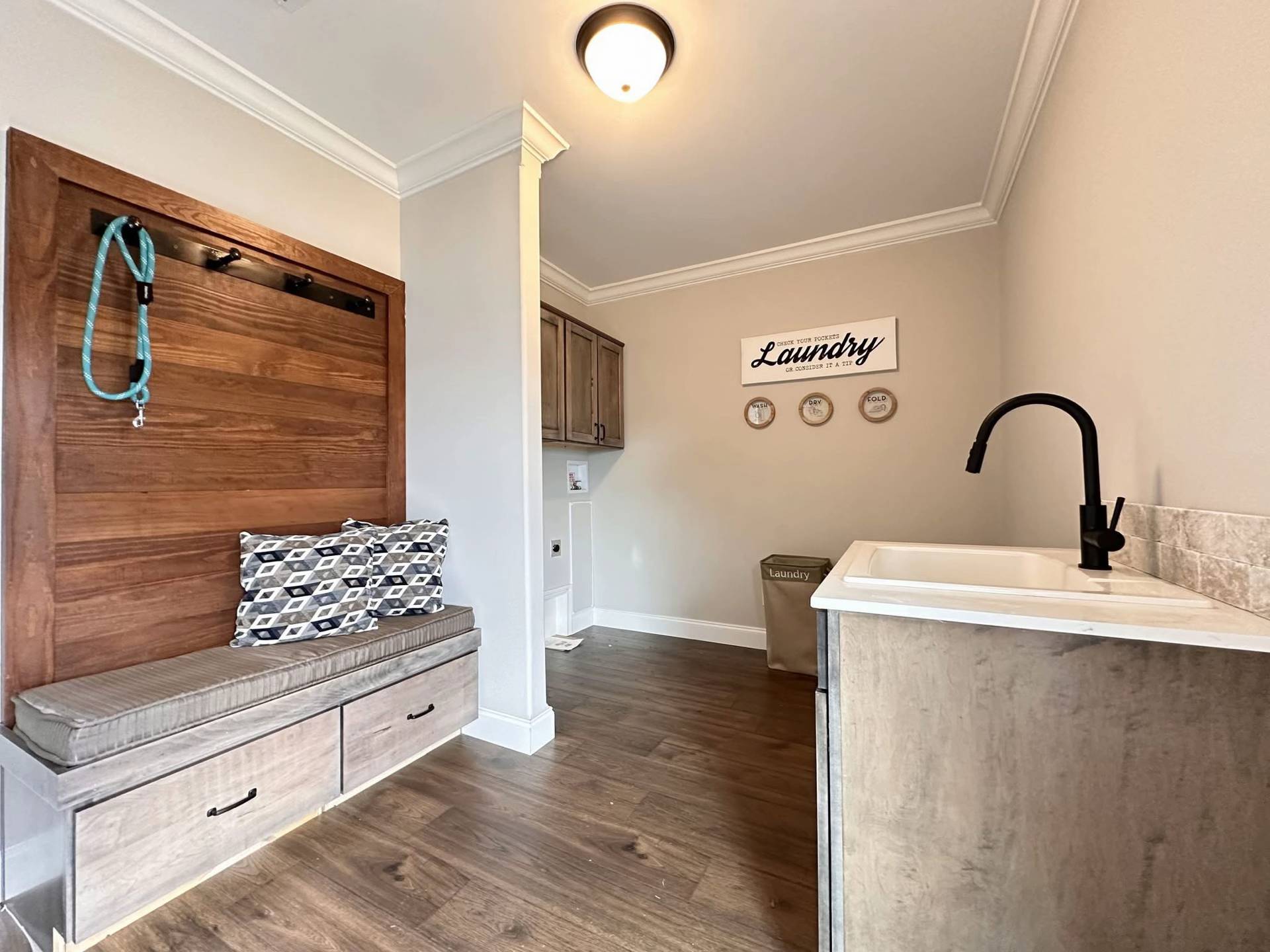Laundry room with a cozy bench and pillows on the left, wooden floor, utility sink with a black faucet on the right, and wall decor reading "Laundry."