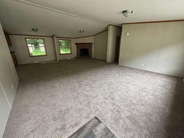Spacious living room with gray carpet, two windows, and a brick fireplace. The room is empty, creating a calm, open atmosphere.