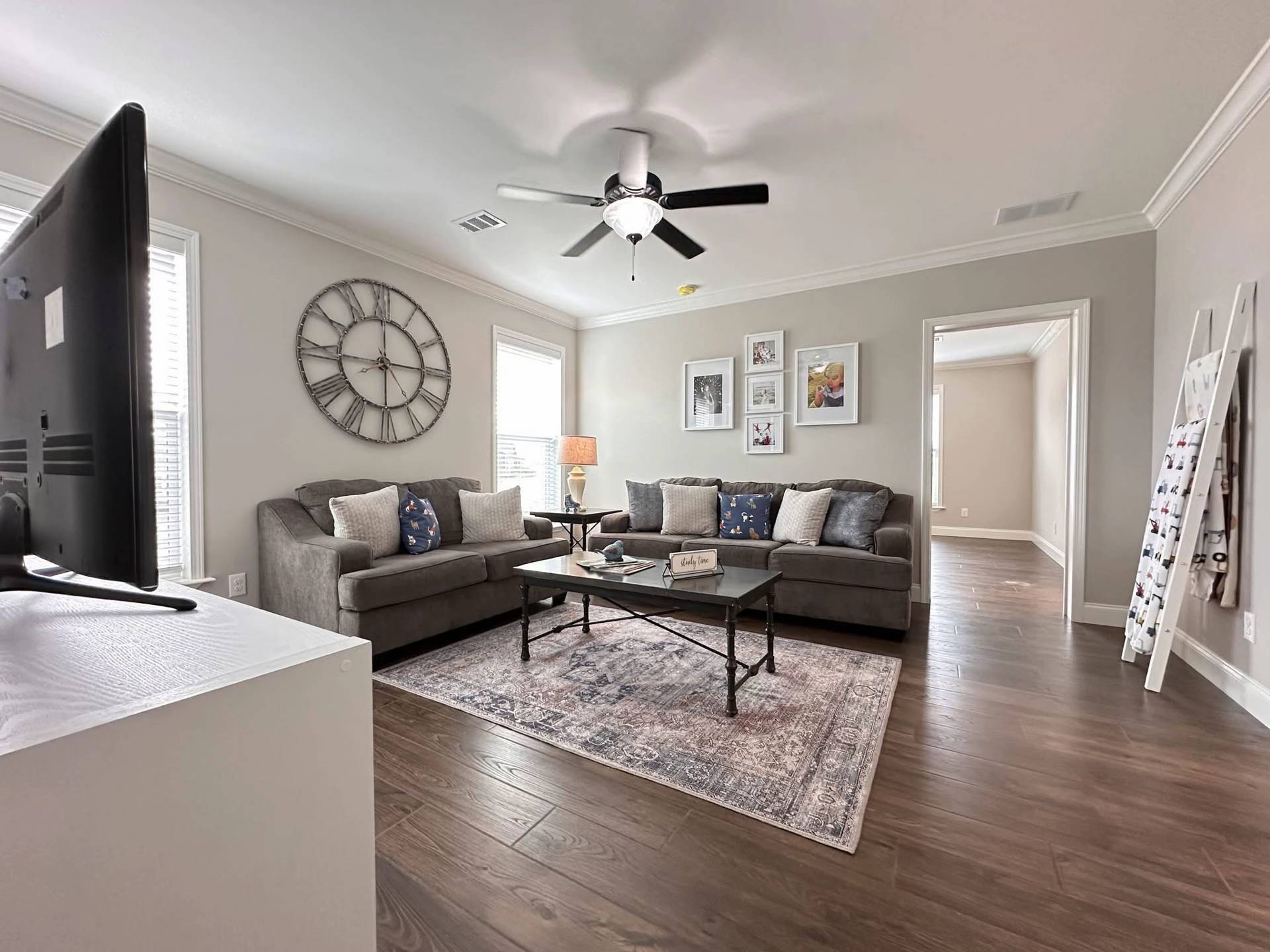 Modern living room with gray sofas, decorative pillows, a coffee table, and a large wall clock. Soft lighting and neutral tones create a cozy ambiance.