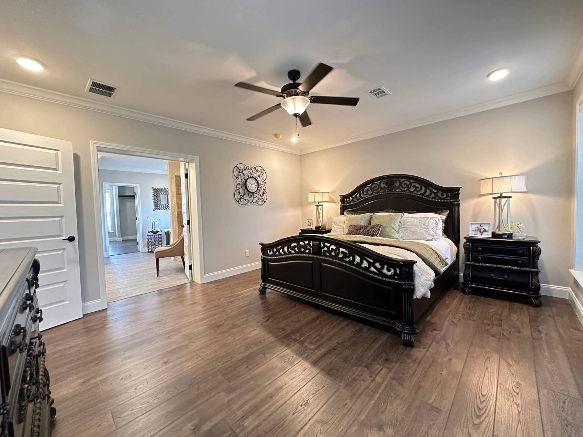 Elegant bedroom with dark wood furniture, a large bed, and neutral tones. A ceiling fan and lamps provide soft lighting. Spacious and inviting.