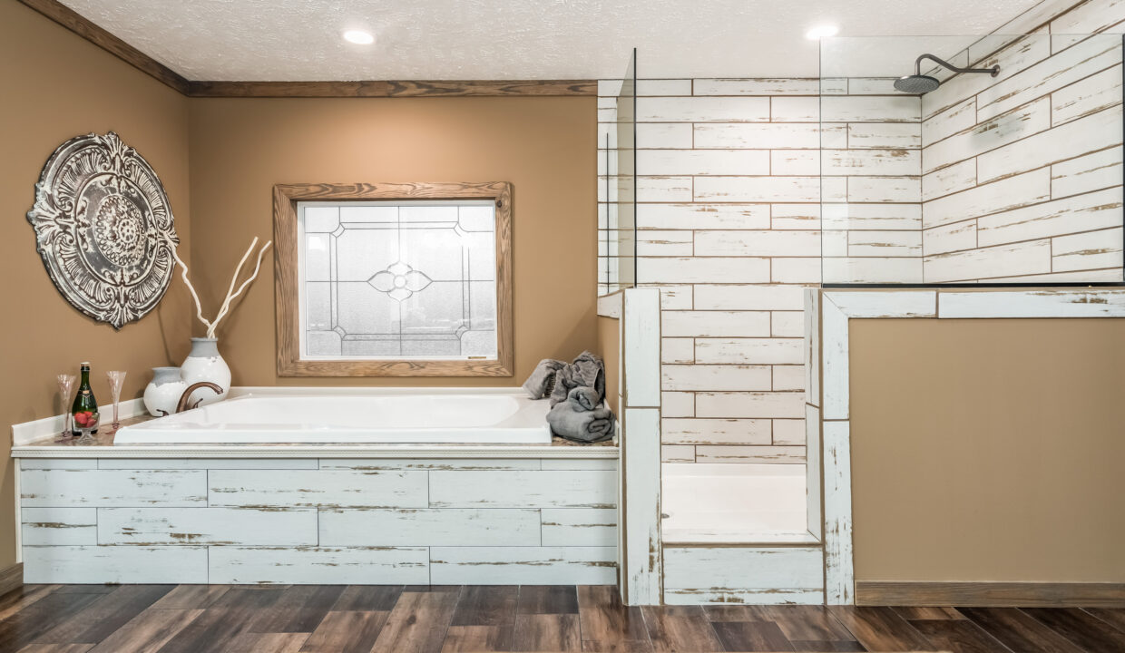 Cozy bathroom with rustic wood accents, featuring a white tub and separate shower. Earth-tone walls, decorative mirror, and wooden floor add warmth.